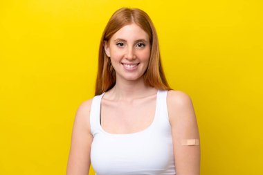 Sarı arka planda izole edilmiş yara bandı takan genç kızıl saçlı kadın çok gülümsüyor.