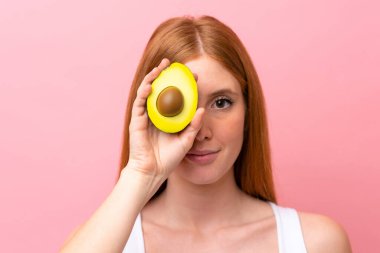 Pembe arka planda izole edilmiş genç kızıl saçlı kadın elinde bir avokado tutuyor. Portreyi kapat