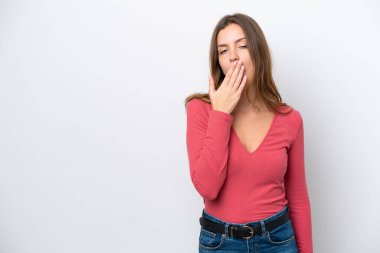 Beyaz arka planda izole edilmiş genç beyaz bir kadın esniyor ve geniş bir ağzı eliyle kapatıyor.