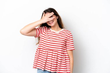 Beyaz arka planda soyutlanmış beyaz tenli genç bir kadın elleriyle gözlerini kapatıyor ve gülümsüyor.