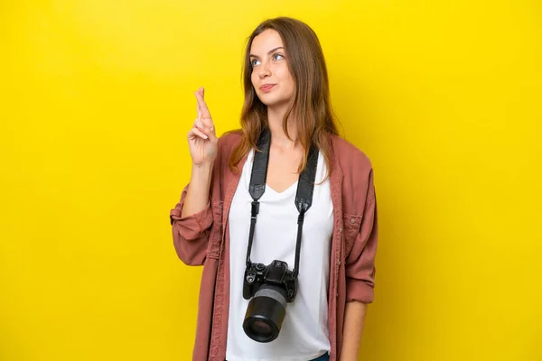 Young photographer caucasian woman isolated on yellow background with fingers crossing and wishing the best