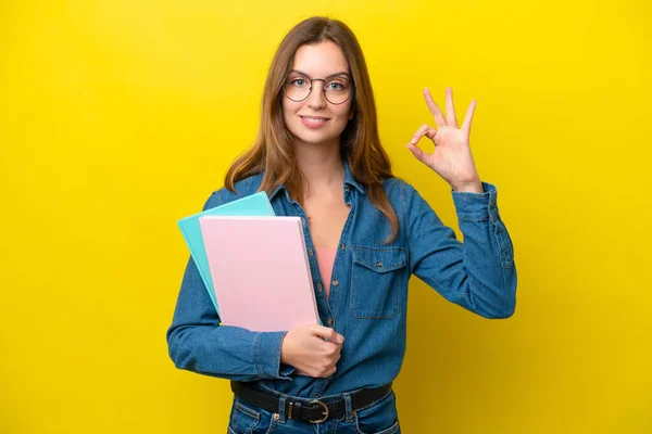 Young student caucasian woman isolated on yellow background showing ok sign with fingers