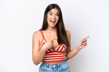 Beyaz arka planda izole edilmiş genç Brezilyalı kadın şaşırmış ve işaret ediyor.