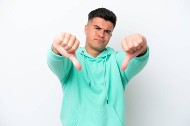 Beyaz arka planda soyutlanmış beyaz tenli yakışıklı bir adam baş parmağını iki eliyle aşağı gösteriyor.