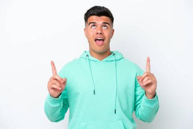 Beyaz arka planda izole edilmiş beyaz, yakışıklı genç adam şaşırmış ve yukarı bakıyor.