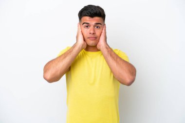 Beyaz arka planda izole edilmiş beyaz, yakışıklı genç adam hayal kırıklığına uğramış ve kulaklarını kapatmış.