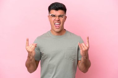 Beyaz tenli yakışıklı adam pembe arka planda izole edilmiş boynuz hareketi yapıyor.