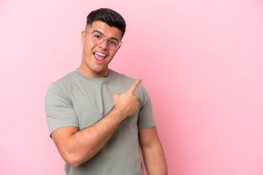 Young caucasian handsome man isolated on pink background surprised and pointing side