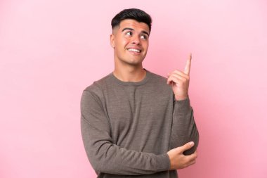 Pembe arka planda izole edilmiş beyaz, yakışıklı genç adam harika bir fikre işaret ediyor.