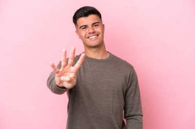 Beyaz tenli yakışıklı adam pembe arka planda izole edilmiş mutlu ve parmaklarıyla dört kişi sayıyor.