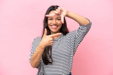 Young Colombian woman isolated on pink background focusing face. Framing symbol
