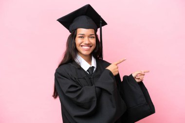 Young university Colombian woman graduate isolated on pink background pointing finger to the side and presenting a product