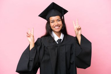 Young university Colombian woman graduate isolated on pink background showing victory sign with both hands