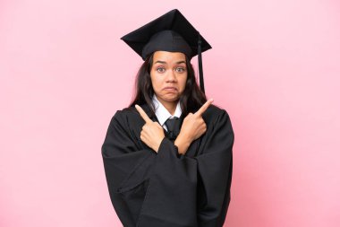 Young university Colombian woman graduate isolated on pink background pointing to the laterals having doubts