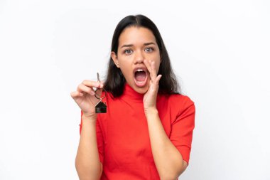 Young Colombian woman holding home keys isolated on white background shouting with mouth wide open