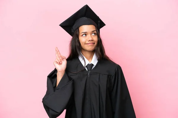Young university Colombian woman graduate isolated on pink background with fingers crossing and wishing the best