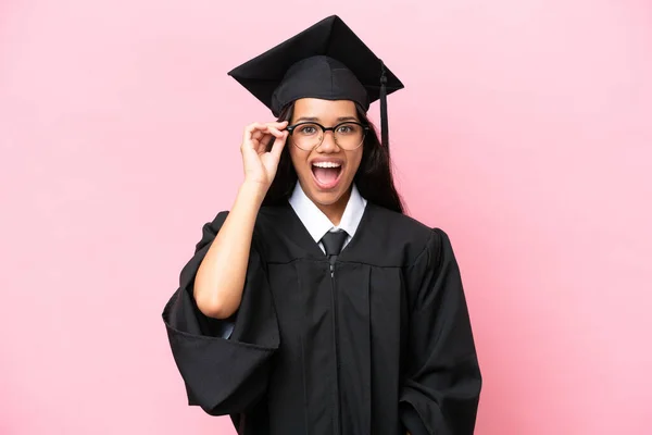 Young university Colombian woman graduate isolated on pink background with glasses and surprised