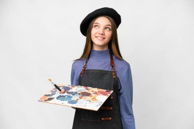 Young artist man holding a palette over isolated white background thinking an idea while looking up