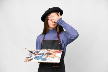 Young artist man holding a palette over isolated white background covering eyes by hands. Do not want to see something