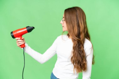 Teenager girl holding a hairdryer over isolated chroma key background with happy expression