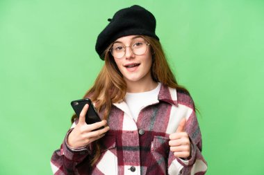 Teenager girl over isolated chroma key background using mobile phone while doing thumbs up