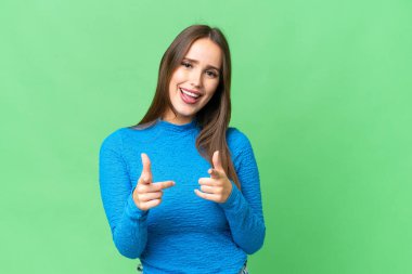 Young beautiful woman over isolated chroma key background pointing to the front and smiling