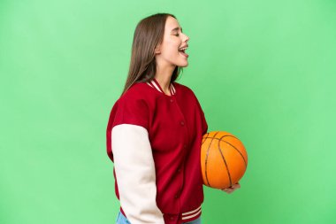 Young beautiful woman playing basketball over isolated chroma key background laughing in lateral position