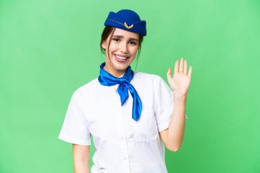 Airplane stewardess over isolated chroma key background saluting with hand with happy expression