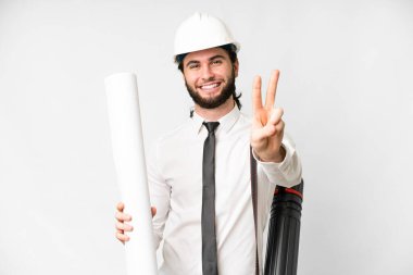 Miğferli genç mimar, izole edilmiş beyaz arka planda planları tutuyor. Gülümsüyor ve zafer işareti gösteriyor.