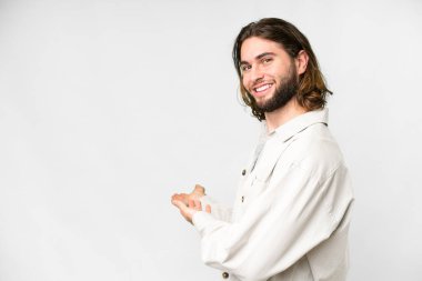 İzole edilmiş beyaz arka planda genç yakışıklı adam davet edilmek için ellerini yana uzatıyor.