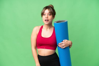 Genç sporcu kız yoga derslerine giderken elinde yalıtılmış krom anahtar arkaplanının üzerinde sürpriz bir yüz ifadesi olan bir minder tutuyor.