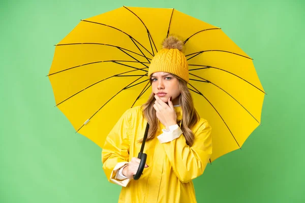 若いです女の子とともにレインプルーフコートと傘上の隔離されたクロマキー背景持っています疑問 — ストック写真