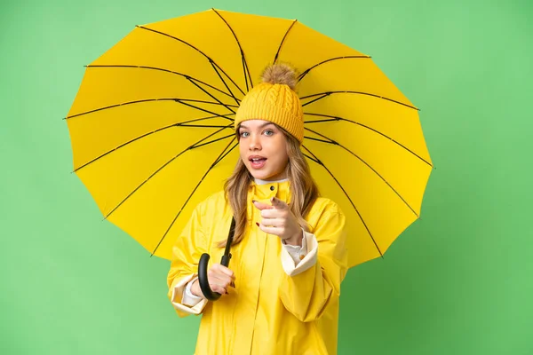 若いです女の子とともにレインプルーフコートと傘上の隔離されたクロマキー背景驚きと指摘フロント — ストック写真