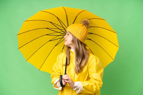穿着防雨外套和雨伞的小女孩在孤零零的彩色关键背景上侧身笑着 — 图库照片