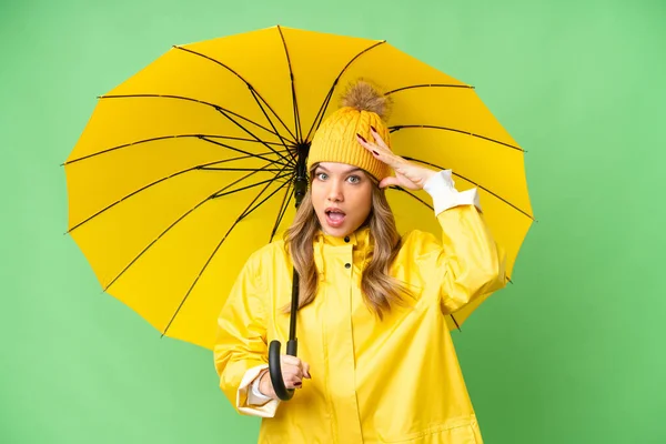 若いです女の子とともにレインプルーフコートと傘上の隔離されたクロマキー背景とともに驚きの表現 — ストック写真