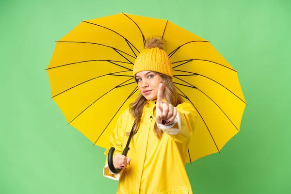 穿着防雨外套 披着雨伞的小女孩 独立的彩色关键背景上露出并举起了一个手指 — 图库照片