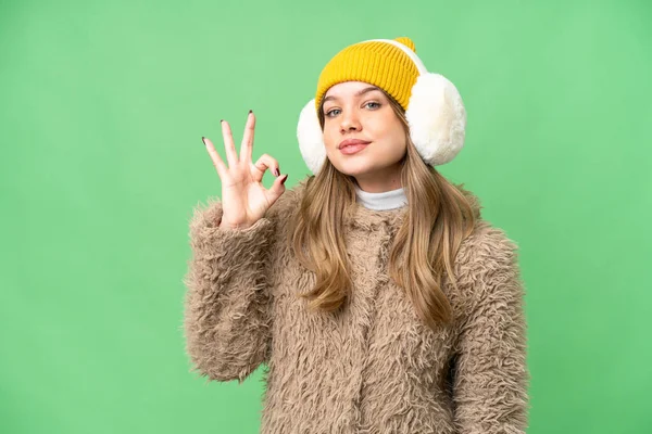 年轻姑娘穿着冬衣 罩在孤立的彩色关键背景上 用手指显示出好的标志 — 图库照片