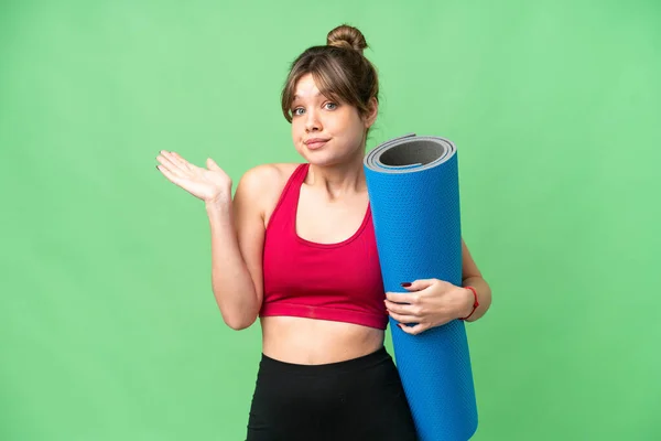 年轻的女运动员一边举手投足 一边拿着垫子去上瑜伽课 上面盖着一个孤立的彩色关键背景 心里充满了疑虑 — 图库照片