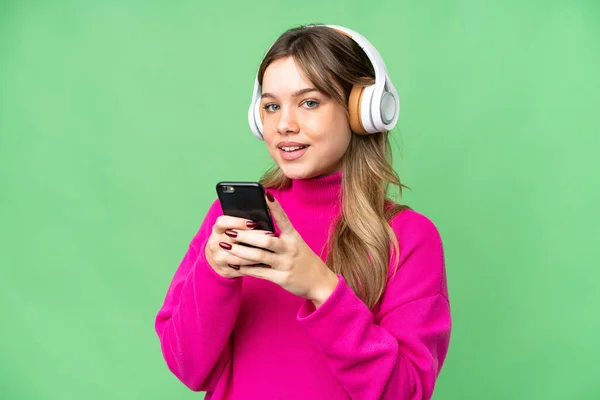 若いです女の子上の隔離されたクロマキー背景リッスン音楽とともにA Mobileと見る前 — ストック写真