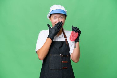 Young caucasian woman wearing an apron and serving fresh cut meat over isolated background happy and smiling covering mouth with hand