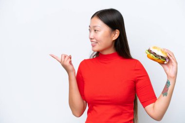 Young Asian woman holding a burger isolated on white background pointing to the side to present a product