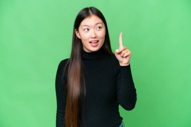 Genç Asyalı kadın izole edilmiş krom anahtar arka planda bir parmağını kaldırarak çözümü anlamaya çalışıyor.