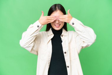 Genç Asyalı kadın izole edilmiş krom anahtar arkaplan gözleri kaplıyor ve gülümsüyor