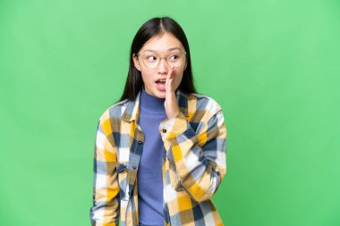 Soyutlanmış krom anahtar geçmişi olan genç Asyalı kadın yan tarafa bakarken sürpriz bir jest yaparak bir şeyler fısıldıyor.