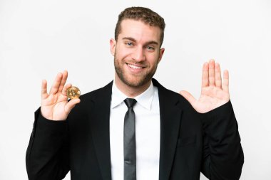 Genç bir iş adamı elinde Bitcoin ile izole edilmiş beyaz bir arkaplanda mutlu bir ifadeyle selam veriyor.