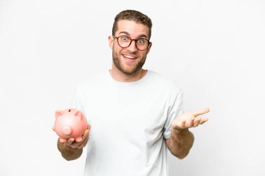 Yüzünde şok ifadesi olan bir kumbara tutan yakışıklı sarışın adam.