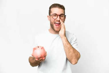 Genç yakışıklı sarışın adam kumbarayı tutuyor ve ağzı açık bağırıyor.