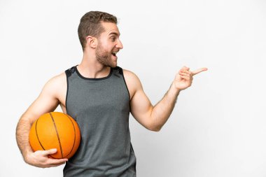 İzole edilmiş beyaz arka planda basketbol oynayan yakışıklı genç adam parmağını yana uzattı ve bir ürün sundu.