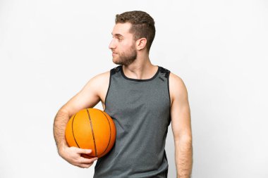 İzole edilmiş beyaz arka planda basketbol oynayan yakışıklı genç adam yan tarafa bakıyor.