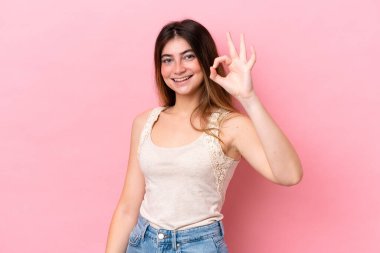 Pembe arka planda izole edilmiş beyaz bir kadın parmaklarıyla tamam işareti gösteriyor.